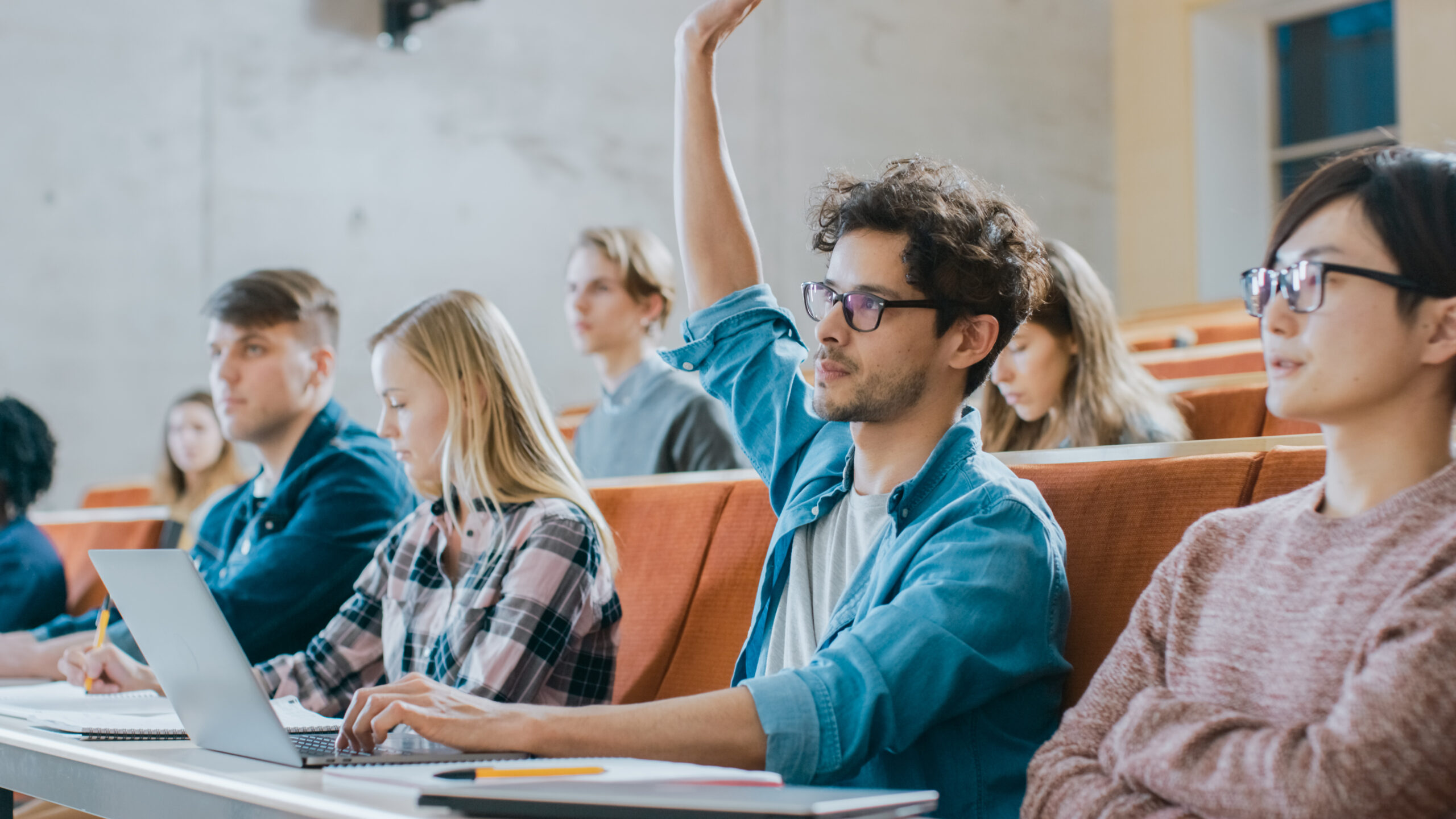 College student raising hand in lecture hall.